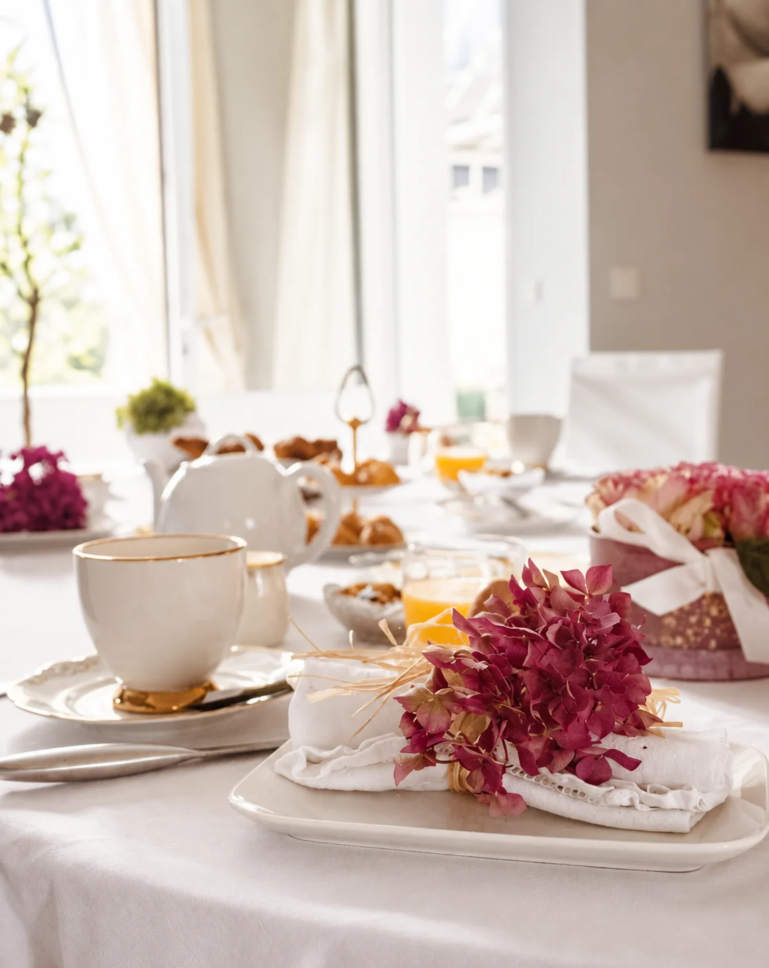 Vaisselle blanche et fleurs roses sur la table du petit-déjeuner près de la fenêtre